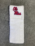 A white terry cloth towel with 'Ole Miss' embroidered in red and blue on the top, laid flat on a gray textured background.